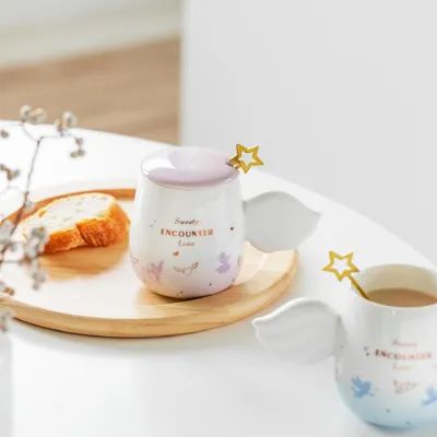 Encantadora taza de cerámica con mangos de alas de ángel y mezcladora de estrella de oro adornada con suaves gradientes de color rosa y azul claro
